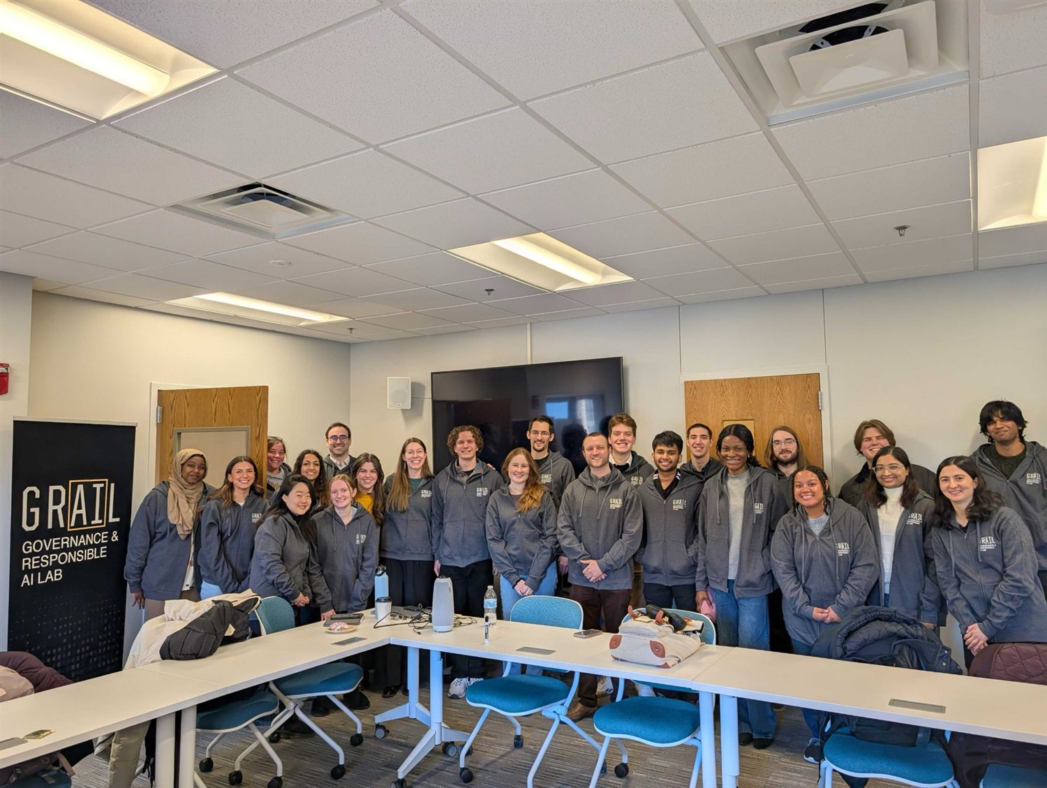 GRAIL lab members standing together in the lab meeting room in front of the GRAIL banner.